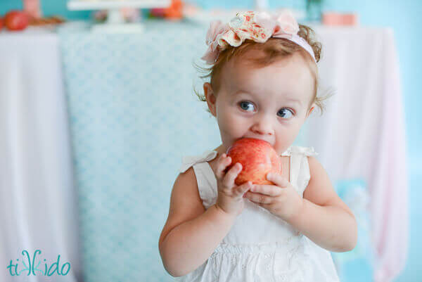 One year old little girl eating an apple