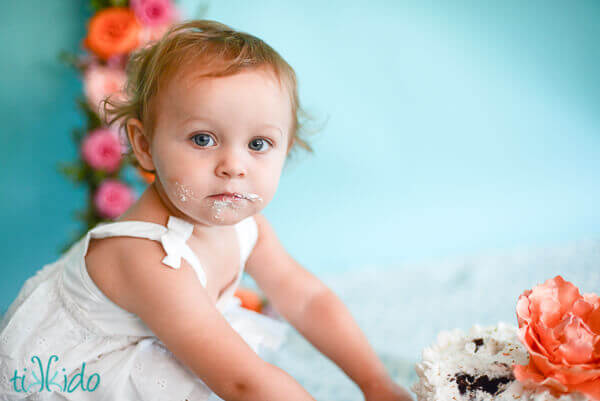One year old little girl with her hands smashing a birthday cake and a face covered in frosting.