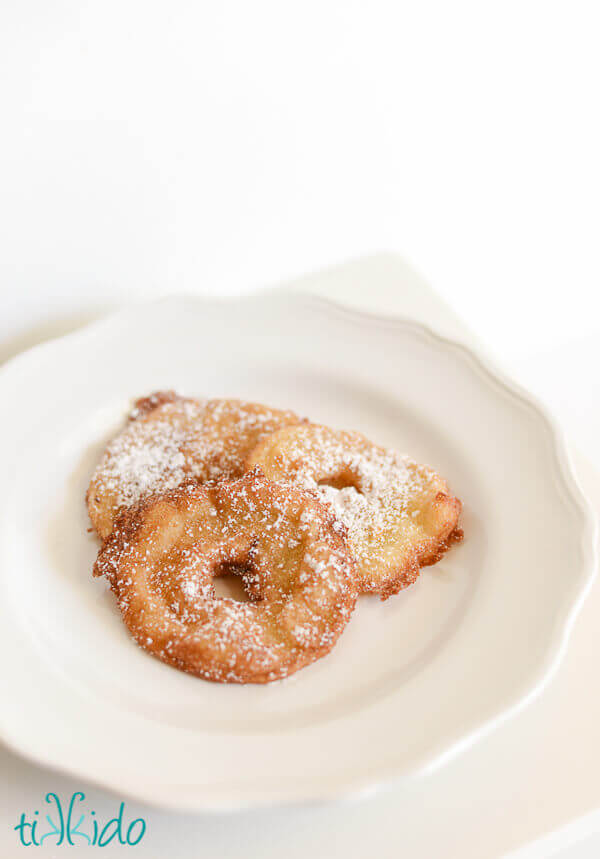 Apple fritter rings dusted with powdered sugar on a white plate.