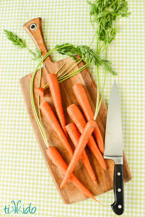 Whole carrots on a wooden cutting board on a green gingham background.