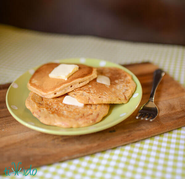 Three carrot cake pancakes topped with pats of melting butter on a green and white polka dot plate.