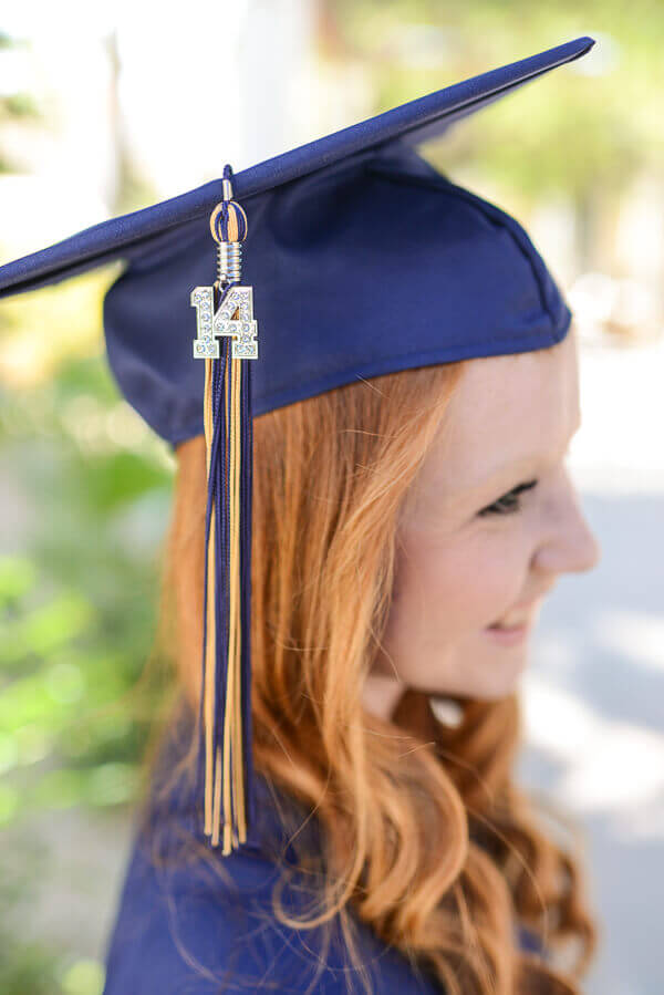 Young woman with red hair wearing a graduation cap with a navy blue and. yellow tassel.