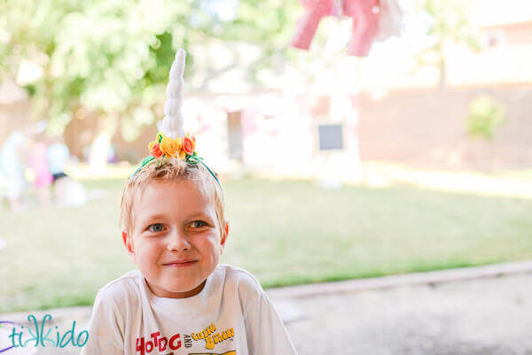 Little boy grinning and wearing a felt unicorn horn headband.