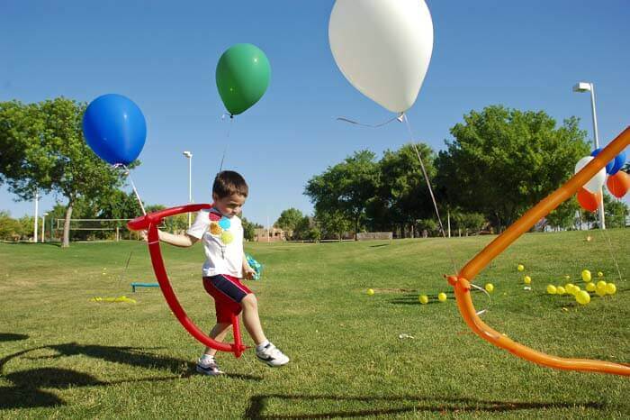 Little boy stepping through a balloon obstacle course at a balloon themed birthday party at a park.