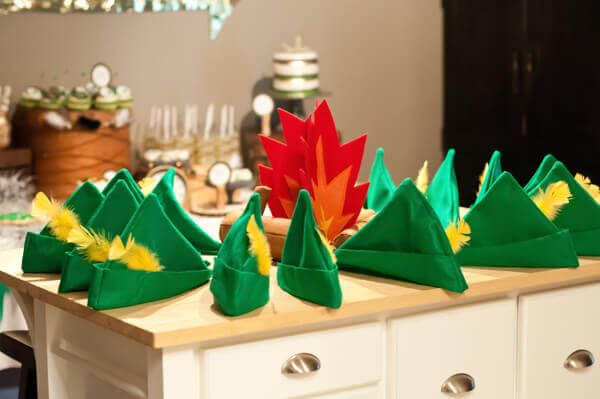 green felt peter pan hats with yellow feathers arranged in a circle around a felt campfire on a table.
