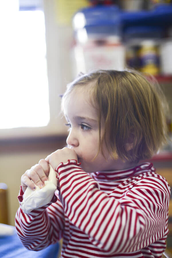 Little girl eating icing directly out of a disposable piping bag.