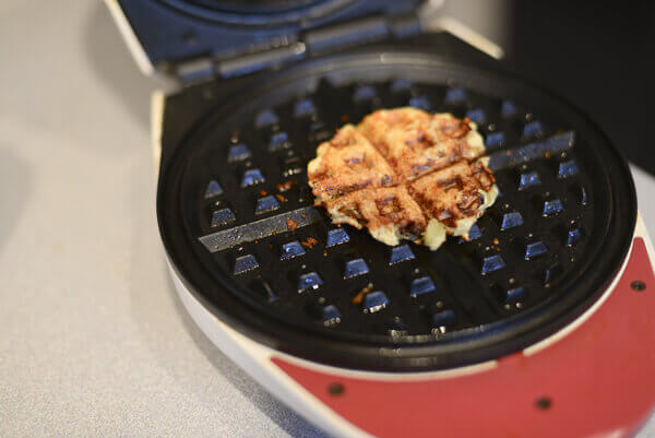 Eggplant slice coated with parmesan cheese being cooked on a waffle iron.