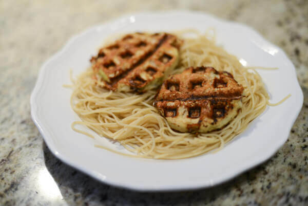Low carb, gluten free, healthy eggplant parmesan made in a waffle iron on a bed of pasta on a white plate.