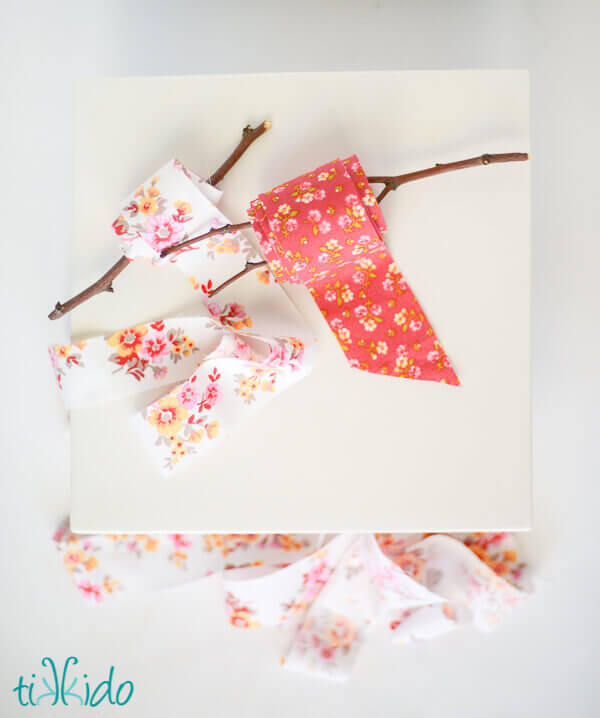 Two spools of DIY fabric ribbon wound around branches on a white background.