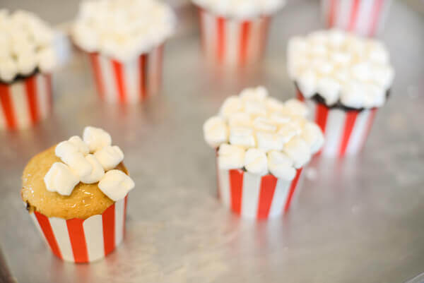 Baked cupcakes in red and white baking cups being covered with mini marshmallows.