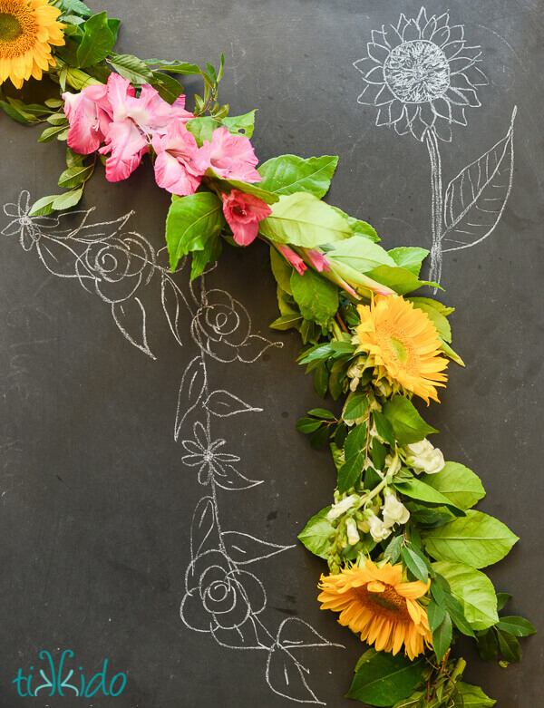 real flower garland on a chalkboard background with sketched flowers.