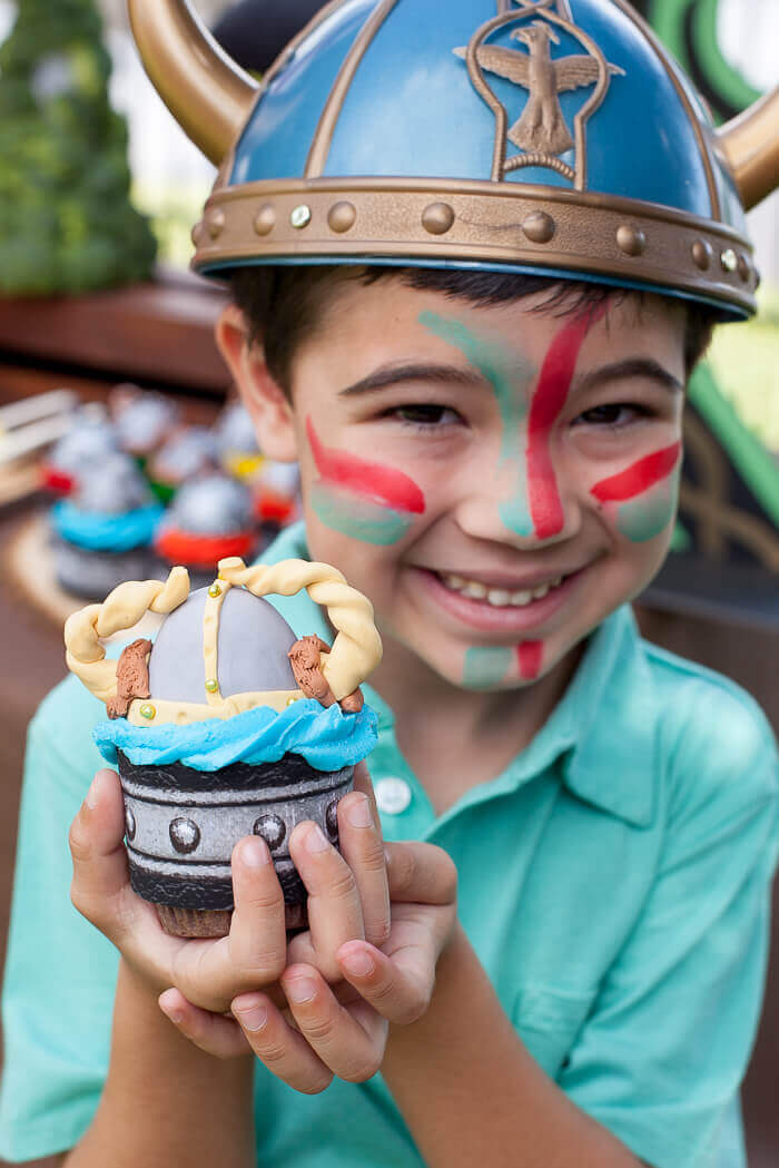 Boy wearing a viking helmet and holding a viking cupcake topped with a gum paste viking helmet.