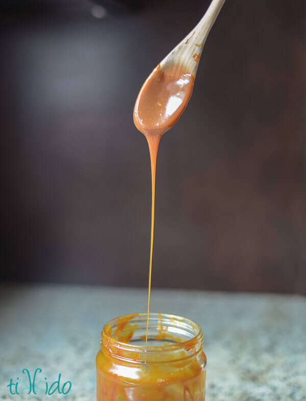 Salted caramel sauce being dripped from a wooden spoon into a glass jar.