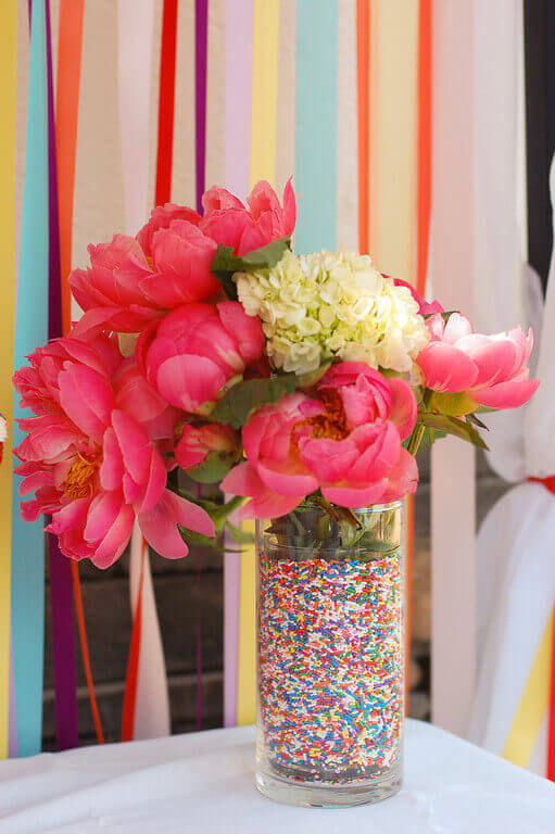 Bouquet of pink and white flowers in a vase that appears to be filled with rainbow sprinkles.