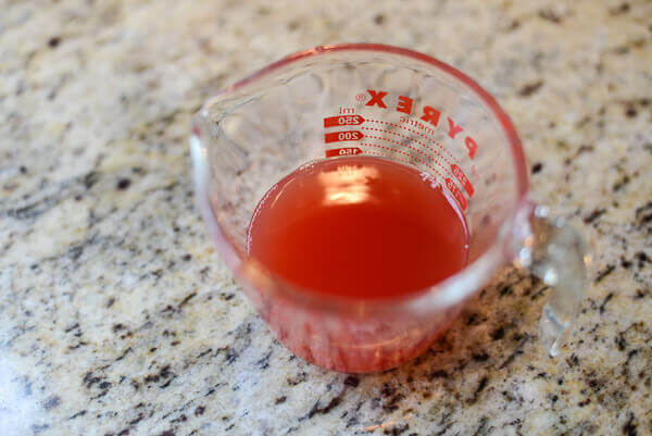 Watermelon juice in a pyrex cup measure on a granite surface.
