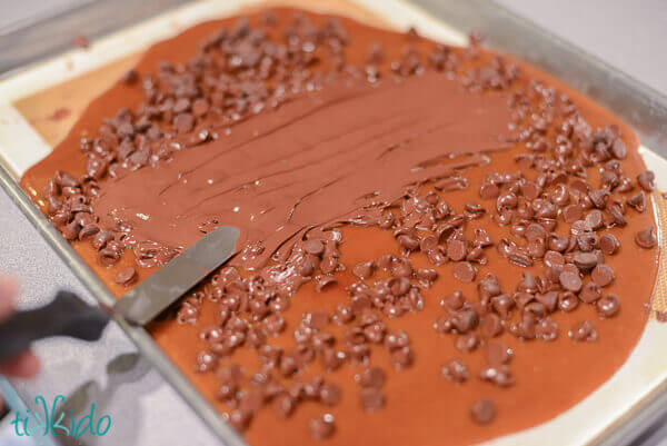 Melted chocolate chips being spread over homemade English toffee