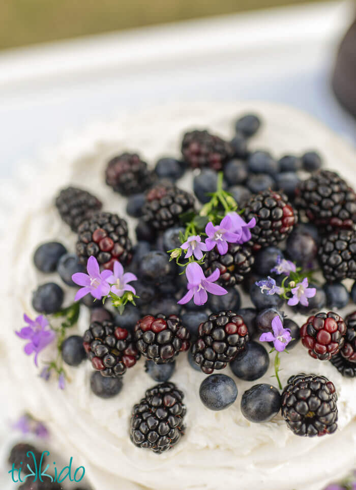 Pavlova layered like a layer cake, topped with whipped cream, blackberries, blueberries, and edible flowers.