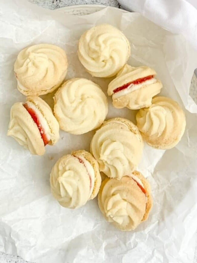 Gluten free viennese whirl sandwich cookies with strawberry jam and buttercream, in a parchment paper lined dish.