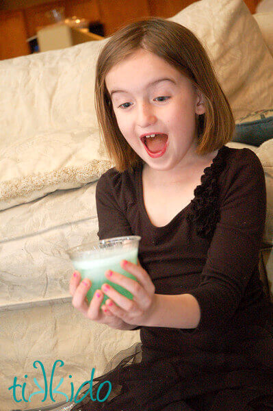 Girl smiling with delight as her clear cup of liquid turns green in her hands.