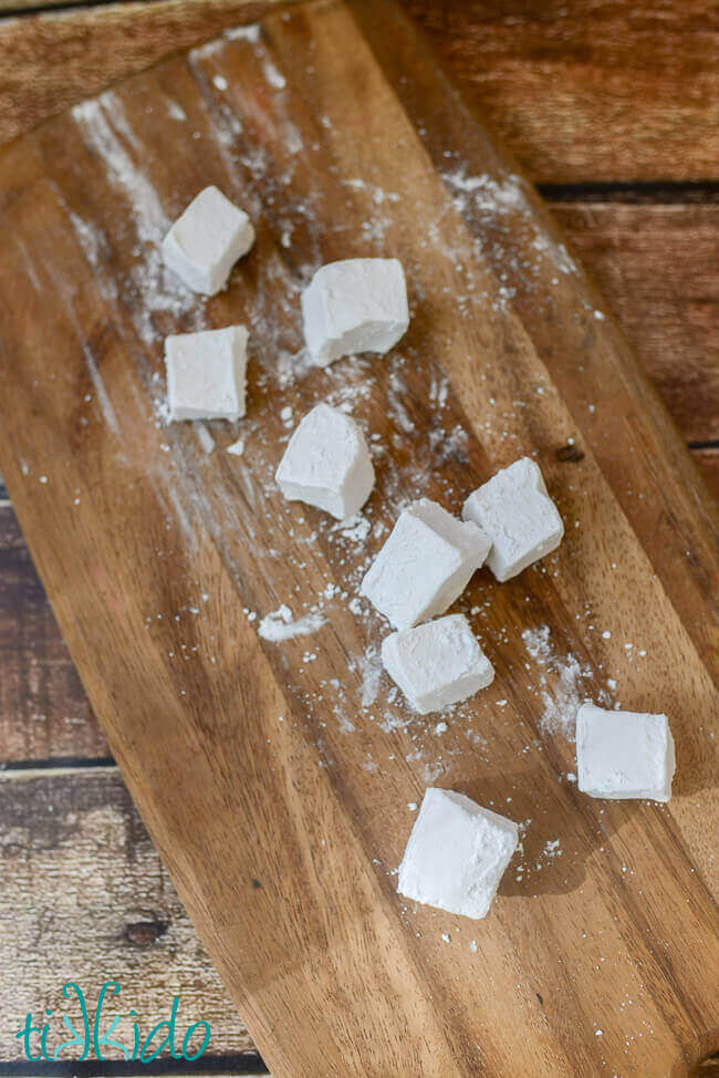 Homemade marshmallows cut into squares and dusted with powdered sugar on a wooden cutting board.