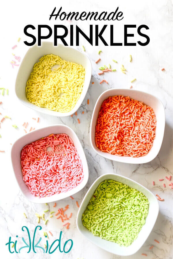 Yellow, orange, pink, and green homemade sprinkles in white bowls on a white marble background.