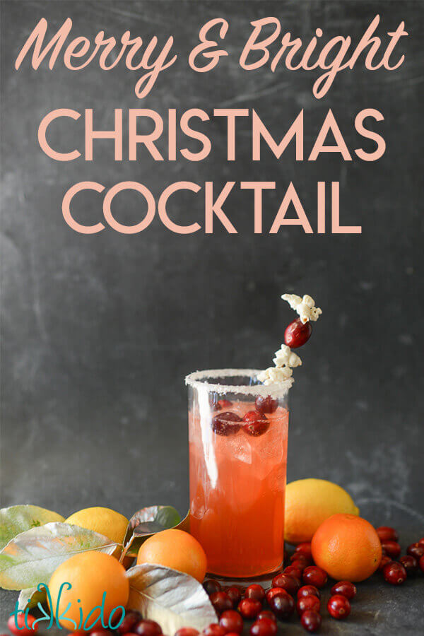 Citrus Christmas Cocktail in a tall glas garnished with a stir stick strung with popcorn and fresh cranberries.  Text overlay reads "Merry and Bright Christmas Cocktail."  Fresh lemons, oranges, and cranberries surround the cocktail glass.