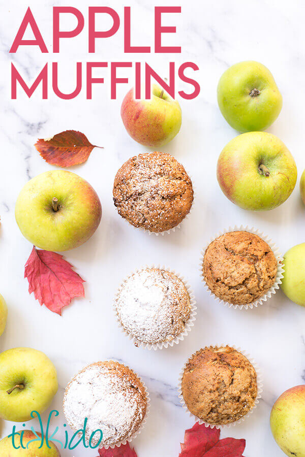 apple muffins surrounded by fresh apples and fall leaves on a white marble background.