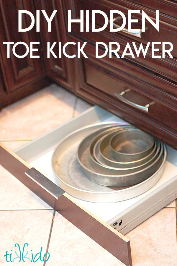 Cake pans in a toe kick drawer under brown kitchen cabinets.