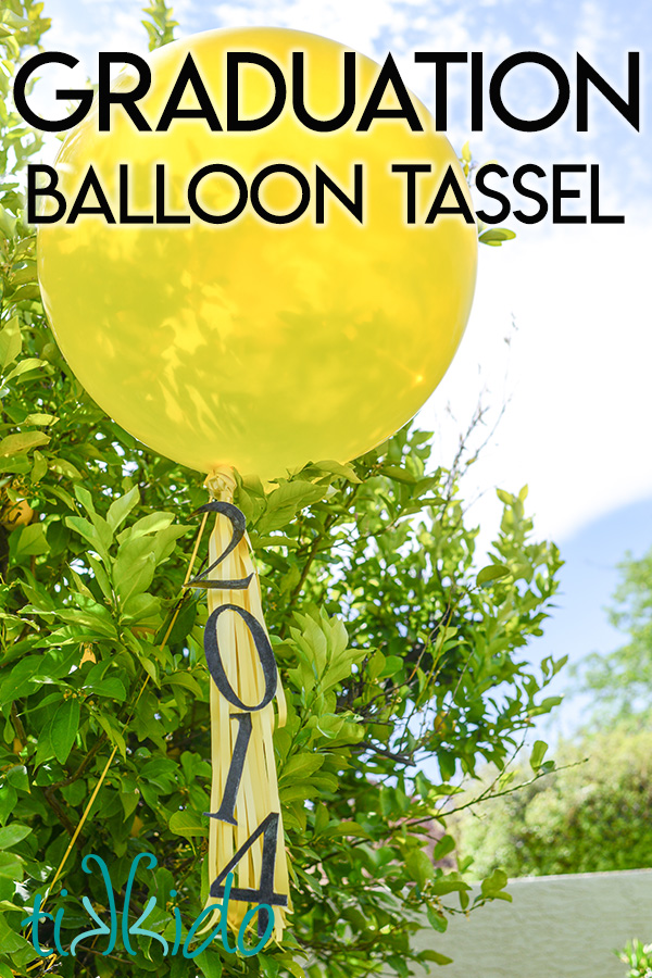 Yellow balloon with graduation balloon tassel floating in front of a tree.
