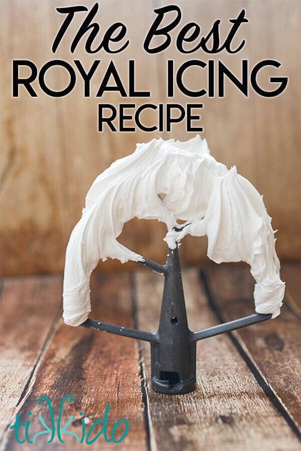 Royal icing on a metal beater standing on a wooden surface.