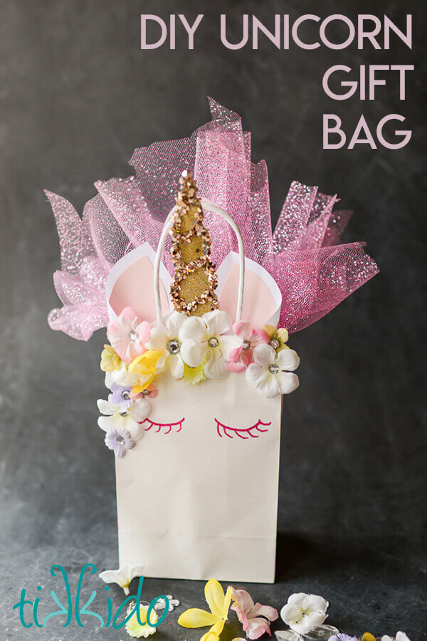 Unicorn Gift bag made out of a plain white paper gift bag, with a flower and rhinestone mane, glittery horn, paper ears, and sparkling tulle sticking out of the bag.