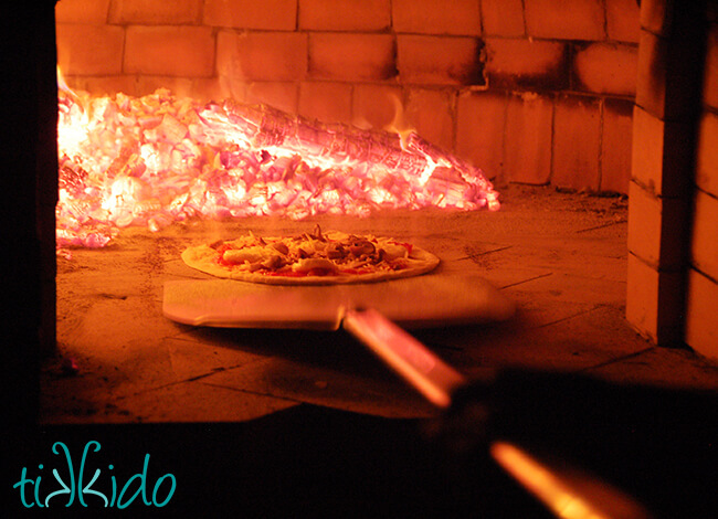 Neapolitan pizza being placed in a wood fired pizza oven with a placing peel.