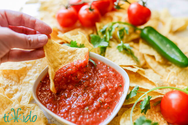 Tortilla chip dipping into a bowl of homemade red salsa.