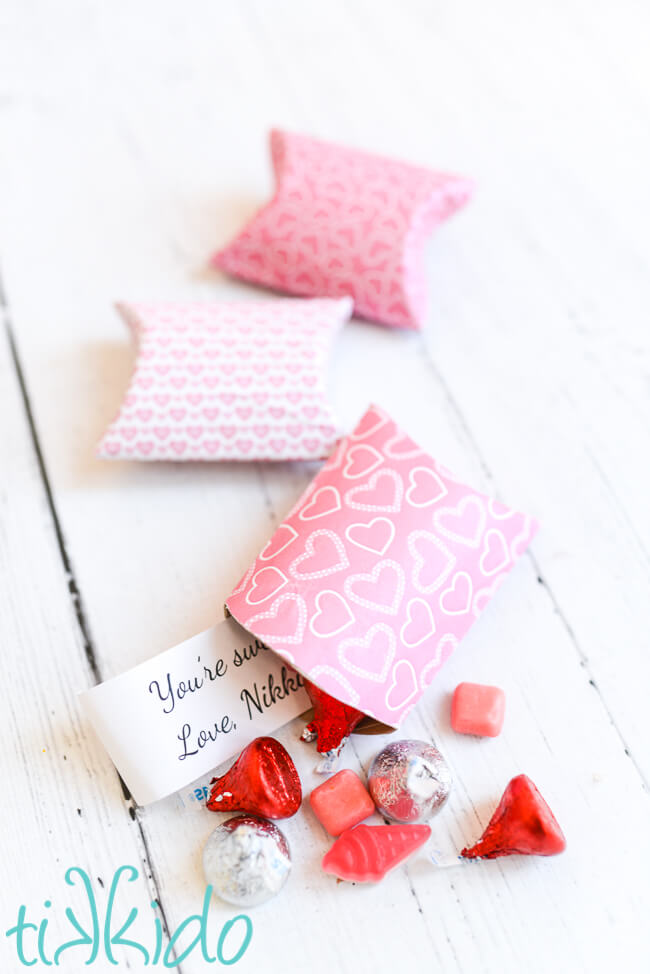 Three valentine's day pillow boxes made from toilet paper rolls, pink and red candy and a note spilling from the pillow box in the foreground.