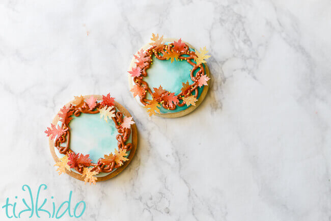 Two fall wreath sugar cookies on a white marble background