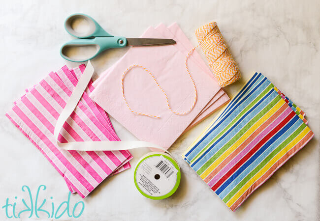 Materials for DIY tassel garland, including paper napkins, baker's twine, ribbon, and scissors.