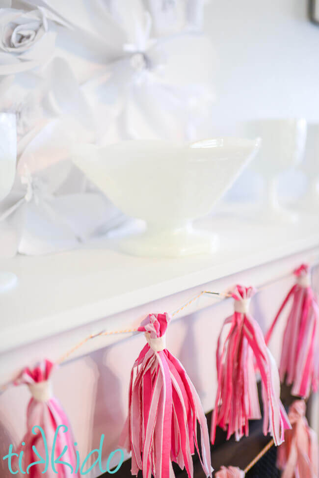 Pink tissue paper tassel garland made from napkins on a white fireplace mantle.