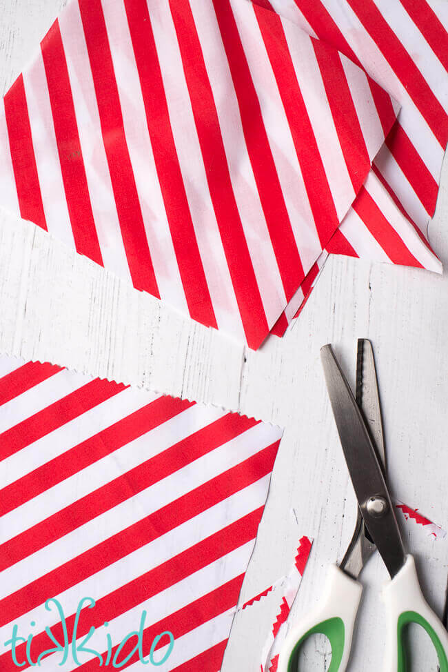 Red and white striped fabric being cut into rectangles with pinking shears for a DIY Advent Calendar.
