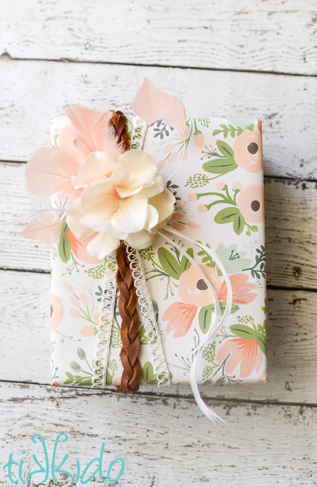 Boho style present, wrapped with floral wrapping paper, and embellished with leather, lace, and a feather and flower gift topper.