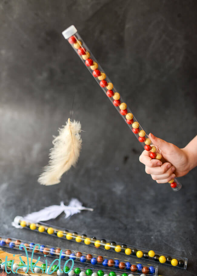 Hand holding candy wand filled with red and gold Gryffindor colors candies, with a feather appearing to levitate in front of the wand.