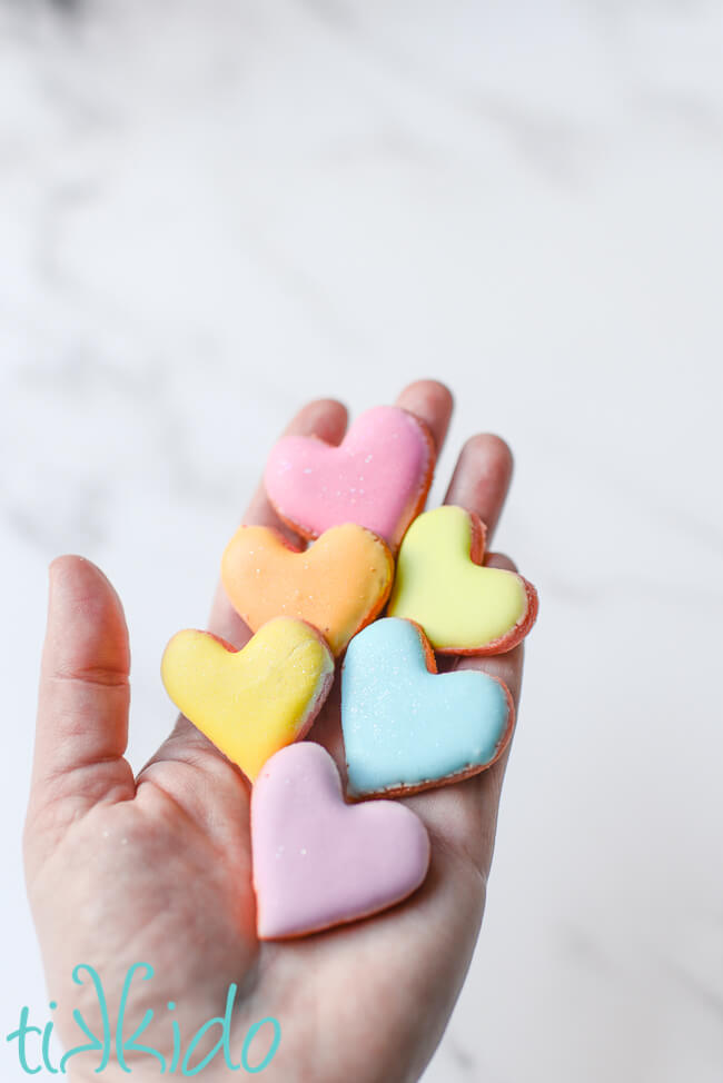 A hand holding six small conversation heart sugar cookies.