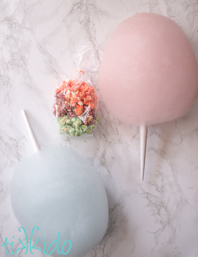 bag of pink, purple, and blue cotton candy popcorn next to two cotton candy cones.