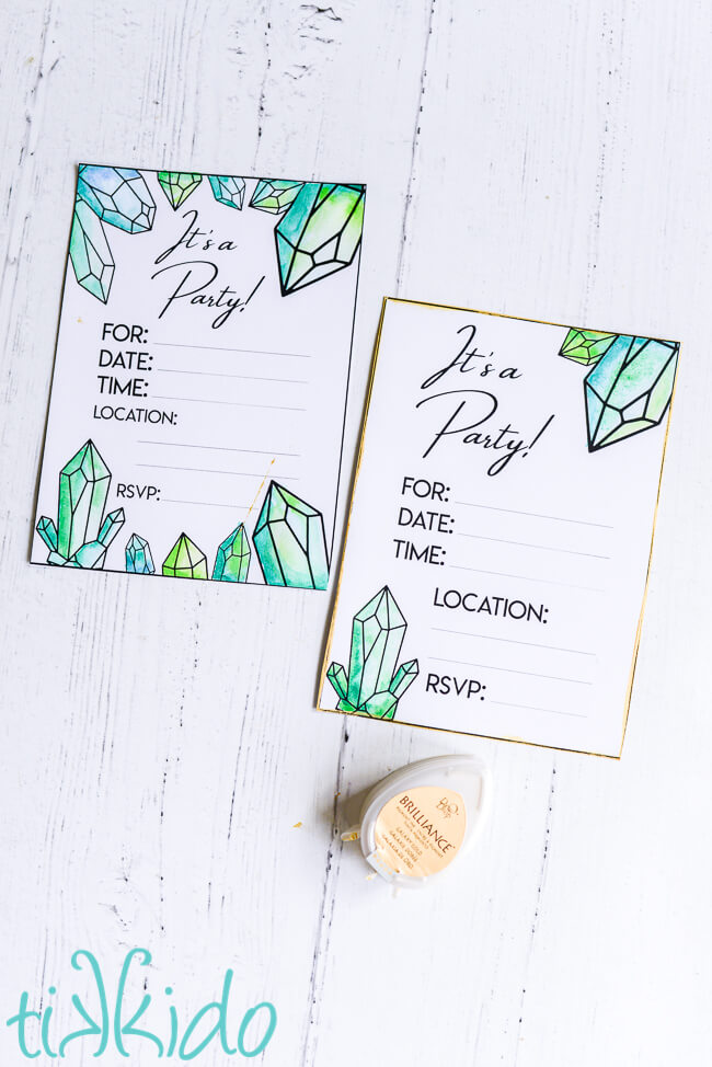 Two printable crystal themed birthday invitations, painted with green watercolor paints.  The invitation on the right features golden edges added with a small gold ink pad sitting below the invitation.