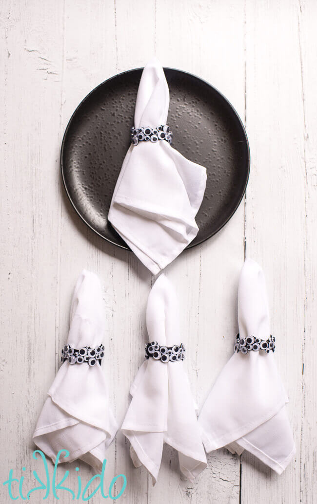 DIY napkin rings made of googly eyes for Halloween on white napkins.