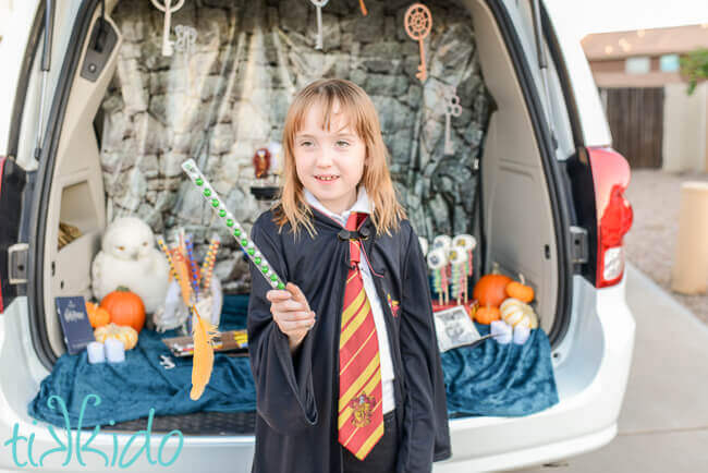 Child holding candy wand filled with green and silver Slytherin colors candies, with a feather appearing to levitate in front of the wand.