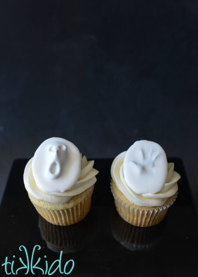 Vanilla cupcakes topped with royal icing and gum paste topper to look like a ghost pushing through a white wall.