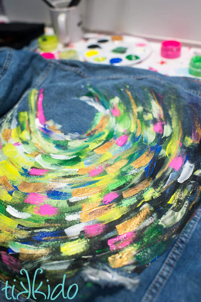 Painted denim jacket painted with bright acrylic paints in an abstract, swirling pattern.
