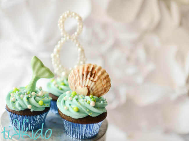 Mermaid and seashell cupcakes in front of a cupcake topped with a number 8 covered in pearls.