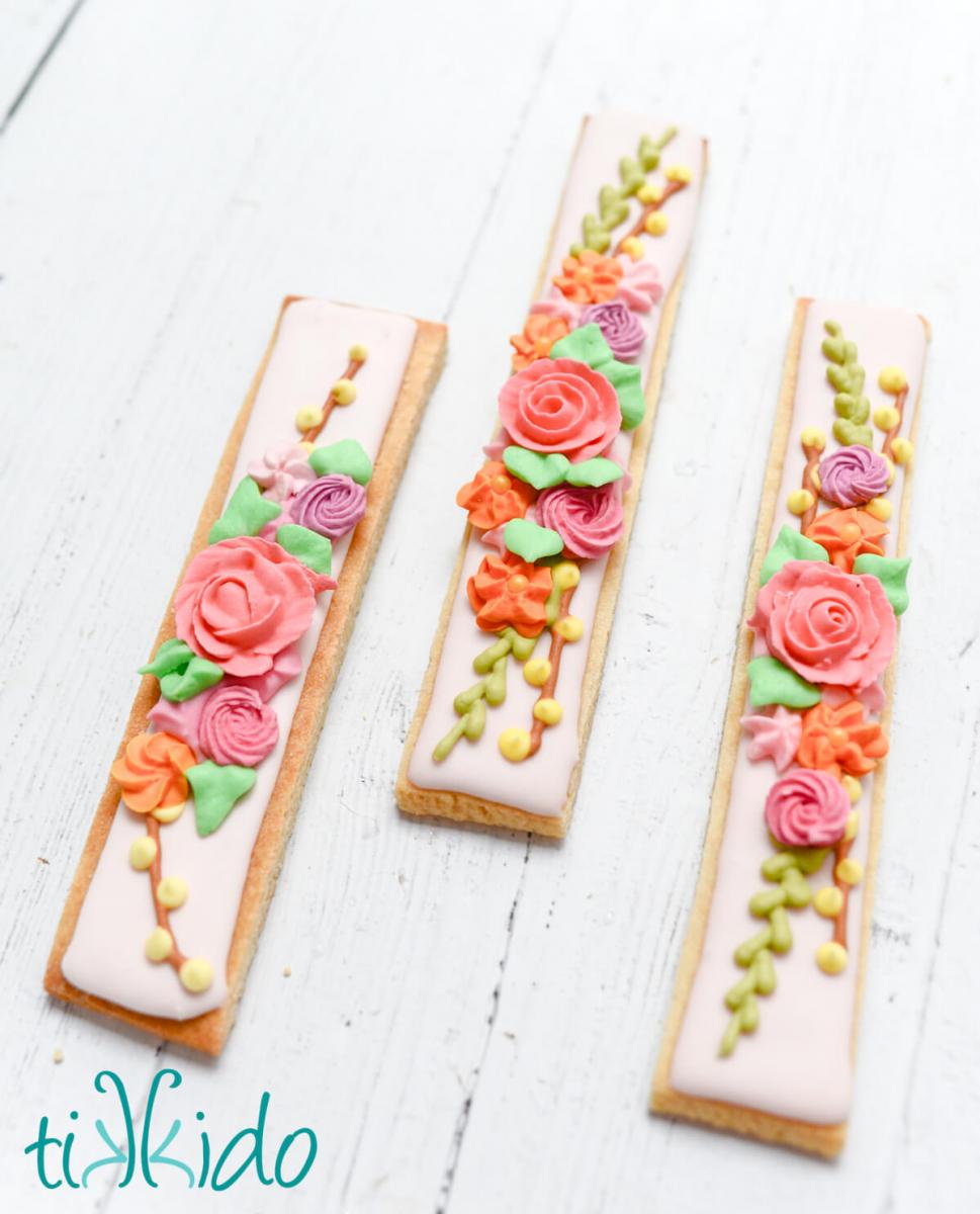 Spring floral cookie sticks arranged on a white wooden surface.