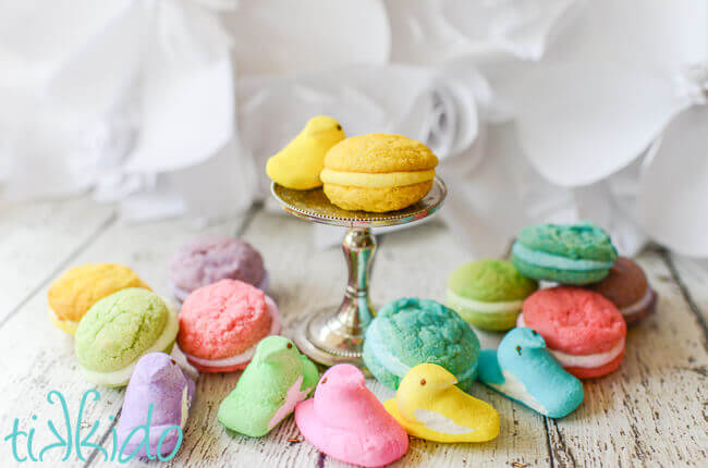 Peeps Whoopie pie sandwich cookie on a tiny metal cake stand, surrounded by Peeps and whoopie pies in assorted Peeps colors.